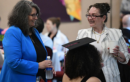 President Milly Peña speaks with one student smiling and the other seen from behind in a grad cap.