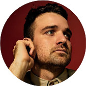 Micah Stock portrait looking to the right on red background