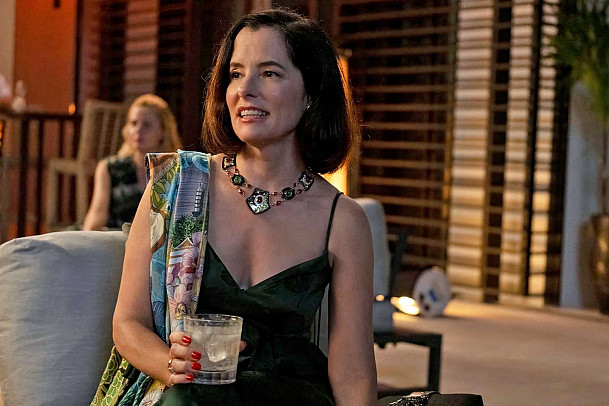 Parker Posey in character holds a drink.
