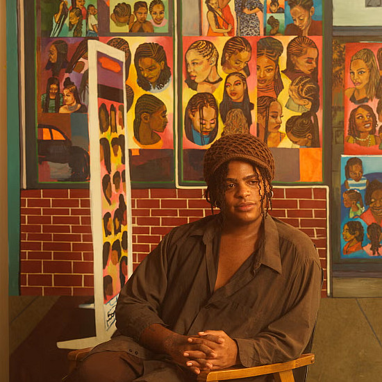 Artist sits in a chair surrounded by brightly colored narrative paintings