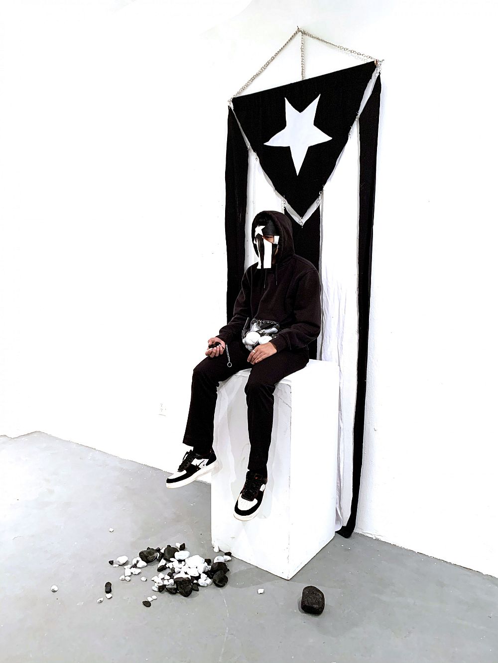 Meila Migdalia, Defense, 2019, Rocks, live performer, black hoodie, vinyl, and flag ©Meila Migdal...