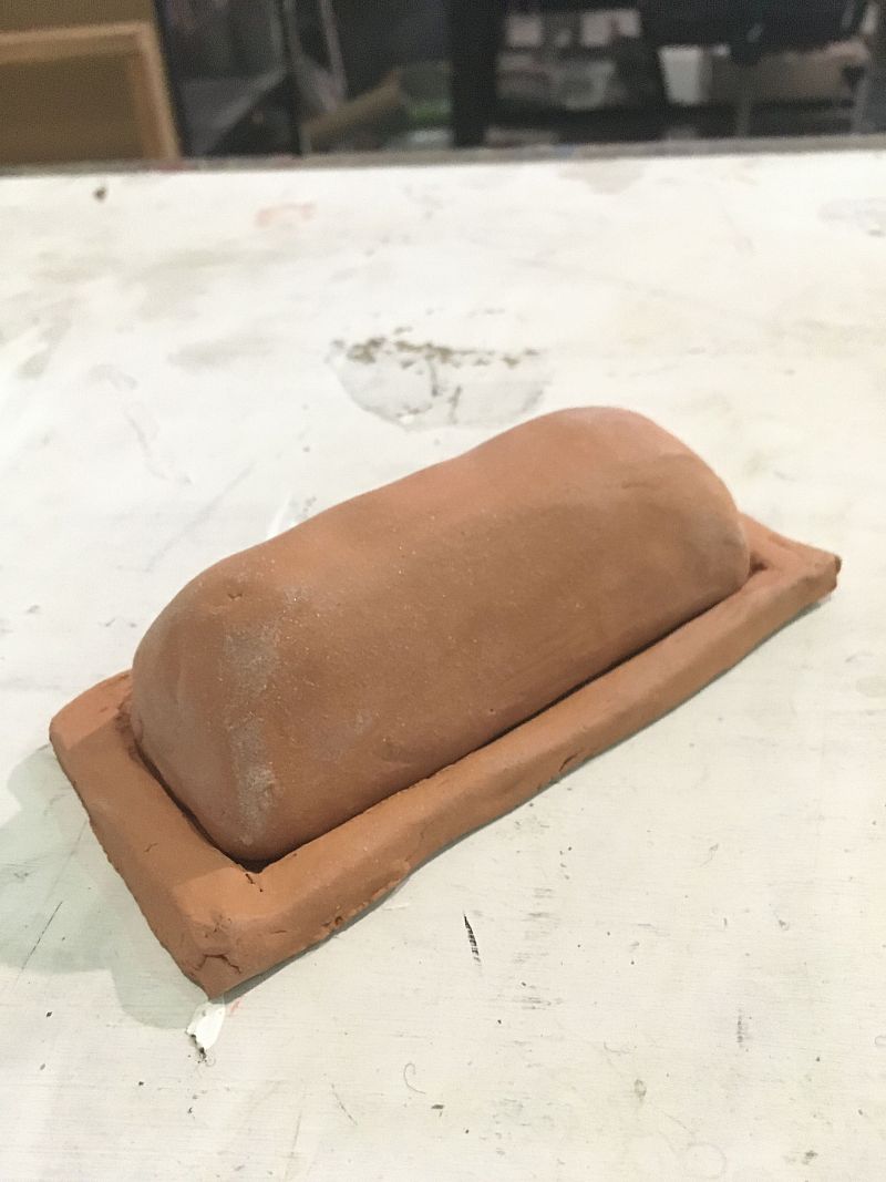Beige Clay sculpture on table in shape of rectangular prism with one piece inside of another piece 