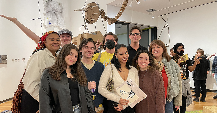 Group of students and professors in a group smiling within an art exhibition.