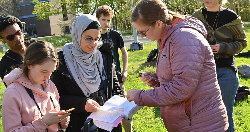 Professor holding a bird looks at a book with students