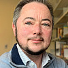 Middle aged white man in a blue sweater with mustache and beard