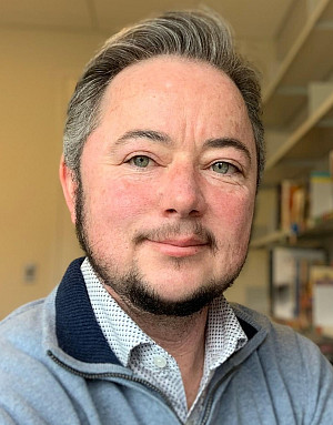 Middle aged white man in a blue sweater with mustache and beard