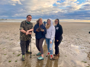 Professor Lisa Jean Moore holds a horseshoe crab with Crispian Thorne '22, Madeline Krol '19, and Anna Hernandez-Krol '15 on Plumb Beach.