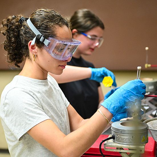 Students in safety goggles working at a chemistry lab bench.