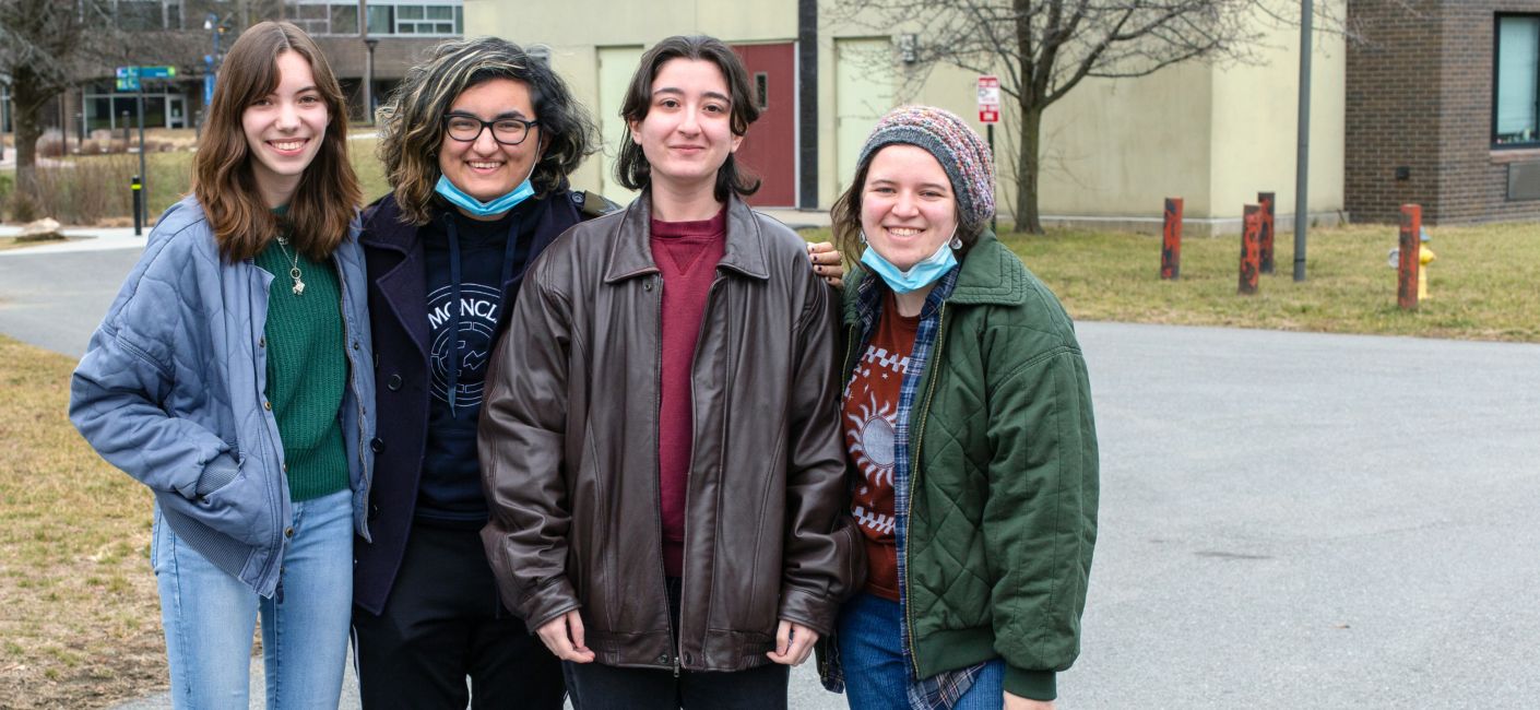 Four people standing together outside on campus smiling.