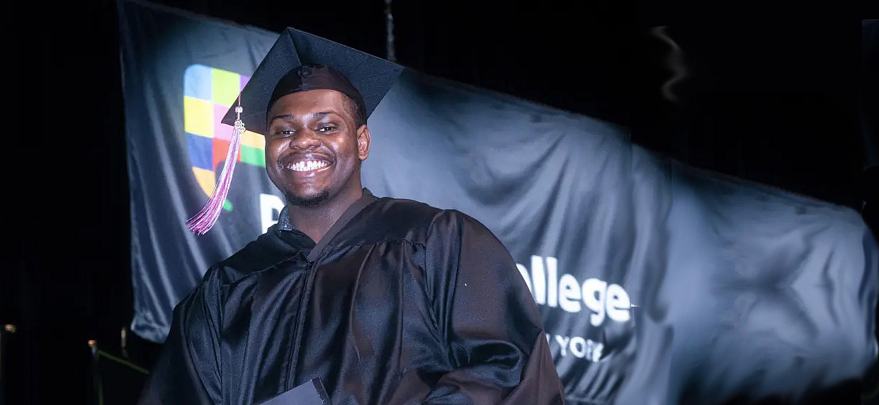 Student in grad cap and gown smiles crossing the stage.
