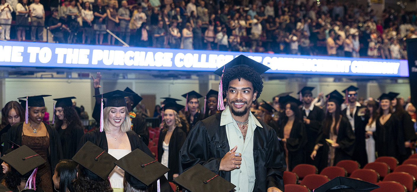 Students in grad caps and gowns enter the seating area.