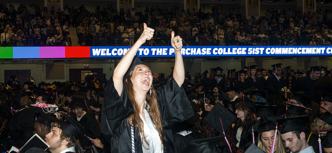 Smiling student in grad cap and gown gives two thumbs up.