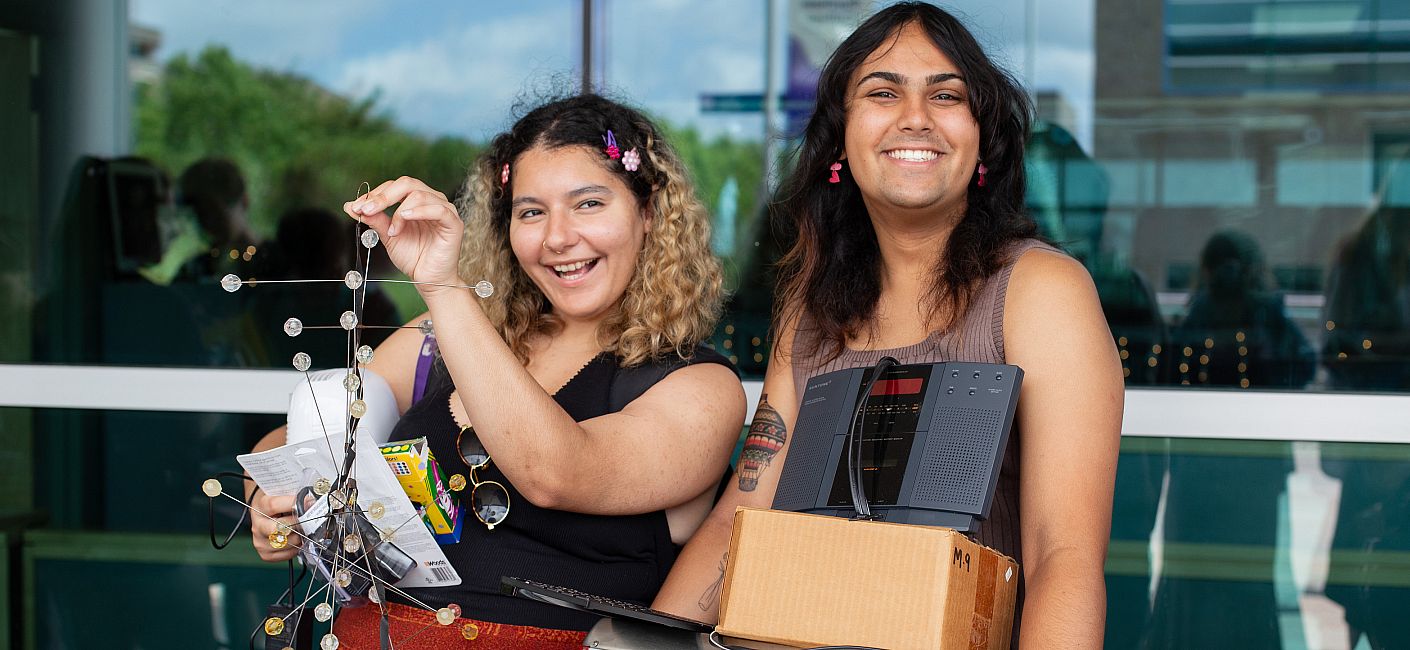 Two students smile and hold goods–a sculpture and a microwave, among others.