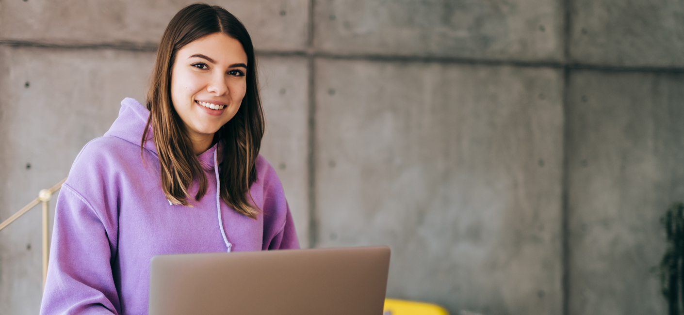 Smiling student in light purple sweatshirt on front of a laptop.