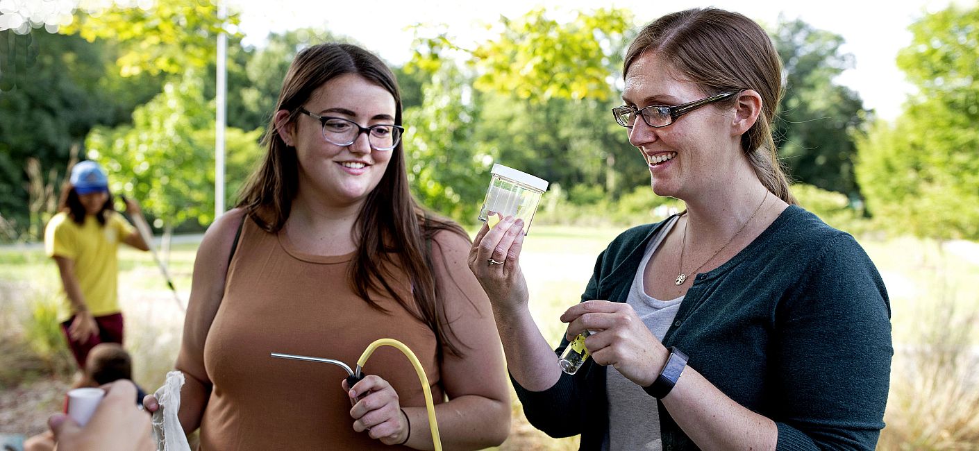 Professor Allyson Jackson at work in the field with a student, both looking at a small container.