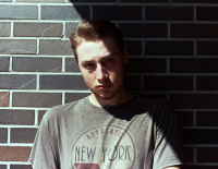 Student stands against brown brick wall with diagonal shadow