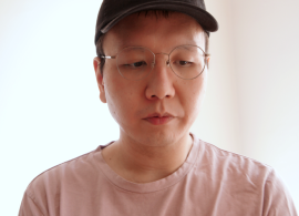 An image of Ryan Kuo in a black hat and pink shirt. Ryan's eyes are looking down and to the side.