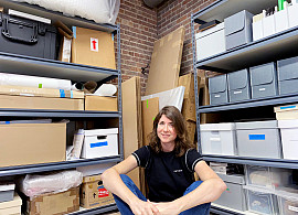 Julia sits in the NYC Department of Records before shelves and an array of boxes and items.