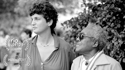 Two people stand close together outdoors, one looking ahead, the other to the side; film festival laurels overlay the black-and-white image.