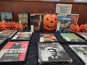 A haunted table display with DVDs and Blu-Rays decorated with Halloween pumpkins.