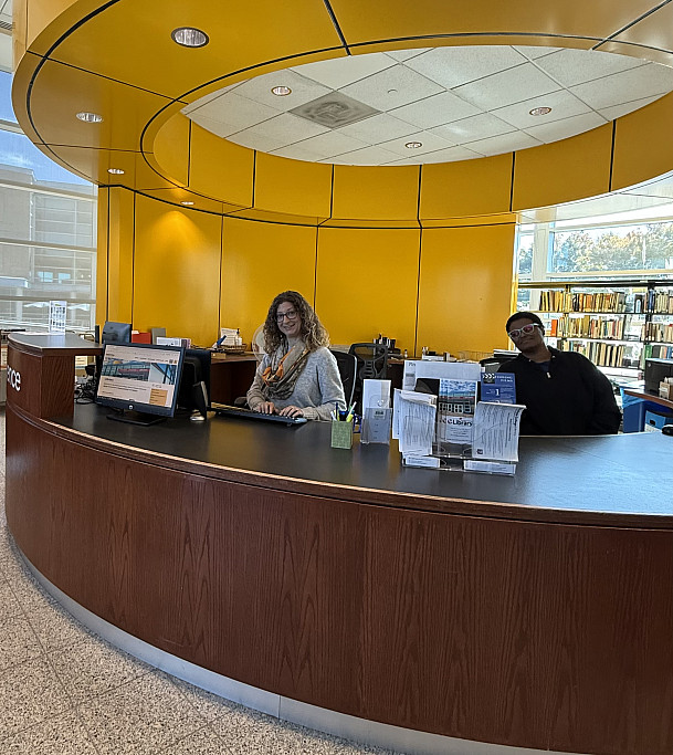 two library staff members sit at a combined reference and circulation service desk